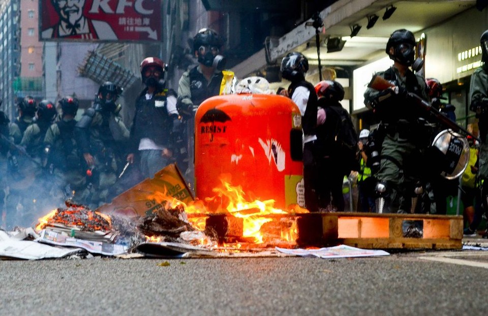 홍콩 경찰과 불타고 있는 시위 잔해들, 잔해 한 가운데에 ‘저항하라’는 마크가 그려져 있다.