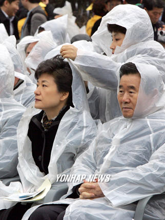 2005년 2월 18일 가랑비가 내리는 가운데 진행된 대구지하철 참사 희생자 추모식에서 한나라당 전여옥 대변인이 박근혜 대표의 비옷에 달린 모자를 씌워주고 있다. (사진 연합뉴스)