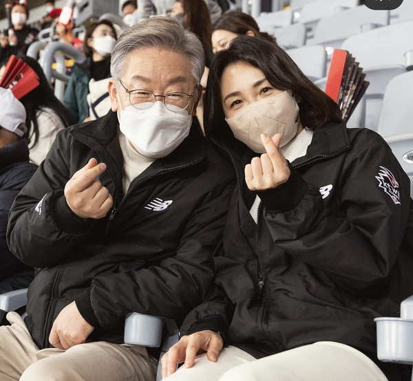 이재명  후보와 김혜경 부부가 야구 관람중 손에 작은 하트를 그리며 다정한 모습을 보이고 있다.(사진=이재명 후보 열린선거캠프)