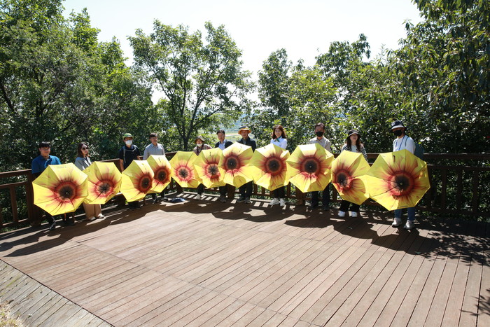 답사 참가자들이 의령 부자축제인 ‘리치리치페스티벌’을 상징하는 해바라기 우산을 쓰고 부잣길을 걸으며 성공적인 축제 개최를 기원하고 있다. ⓒ의령군