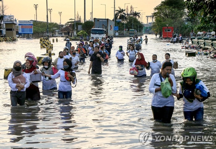 [만조 홍수로 침수된 거리 지나는 인도네시아 해안가 주민들]=6월 20일 인도네시아 중부 자바 스마랑 해안의 탄중 에마스 항구 지역 주민들이 만조 홍수로 침수된 거리를 지나고 있다.