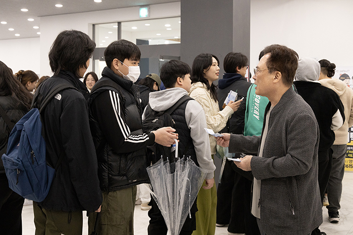 정현태 총장이 식권 발급을 위해 줄을 서 있는 학생들에게 천 원을 나눠주고 있다.(사진=경일대)