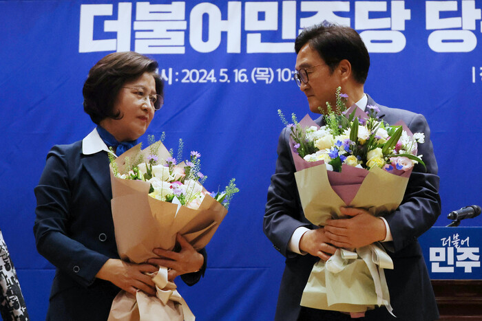 사진: 더불어민주당 국회의장 후보 경선에 나선 우원식(오른쪽)·추미애 후보가 지난 16일 국회 의원회관에서 열린 제22대 전반기 국회의장단 후보 선출을 위한 당선자 총회에서 경선 결과가 발표된 뒤 꽃다발을 들고 서 있다.