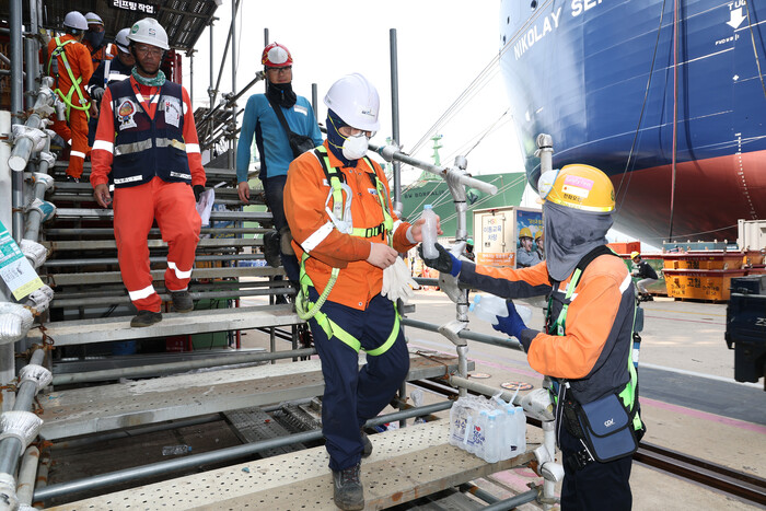 한화오션 안전관리자가 오후 휴식을 위해 작업 중인 배에서 내려오는 작업자들에게 얼음 생수를 전달하고 있다. (사진=한화오션 제공)